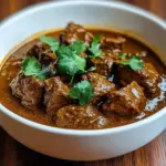 Coconut braised beef curry served in a bowl with herbs and spices.